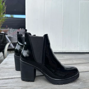 Svarta lackade boots med klack - Snygga svarta chelsea boots i glansigt lackmaterial med bred resår på sidorna och klack. Använda vid ett tillfälle.