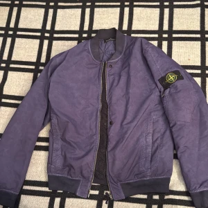 Mörkblå bomberjacka från Stone Island - Säljer en lilla bomberjacka från Stone Island Shadow Project, modell DAVID-TC. Jackan har ribbad krage, dragkedja framtill och klassisk patch på ärmen. Tillverkad i polyester med quiltad insida och två sidofickor. Perfekt för dig som gillar streetwear och snygga detaljer. Storleken är XL men sitter som en M