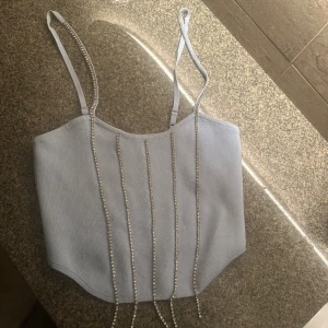 Ljusblå glittrig linnetopp med pärlor - Supersnygg ljusblå linnetopp med justerbara smala axelband och glittriga pärlband som hänger ner framtill. Toppen är croppad och har en rak, något böjd nederkant. Perfekt för att sticka ut passar perfekt med ett par ljusa jeans och klackskor men tyvärr jag har ingen bild , använt en gång.