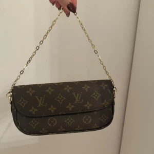 Brun axelväska med monogram - Snygg brun axelväska med klassiskt monogrammönster i brunt. Väskan har guldfärgade metalldetaljer, kedja och justerbar rem som går av i läder med röda och beige inslag. Dustbag och (skadad) låda tillkommer. Helt ny Boxfresh!🧡