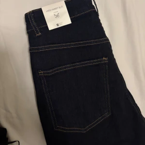 Mörkblå high waist slit jeans stl 36 - Mörkblå jeans från Perfect Jeans i storlek 36 med hög midja och slits nertill på benen. Klassisk femficksmodell med kontrastsömmar och råa kanter vid benslut. Snygg och stilren modell som passar till många olika looks.