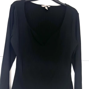 Svart långärmad topp - Svart  topp med lång ärm och djup v-ringning. Snygg detalj med ribbad struktur.