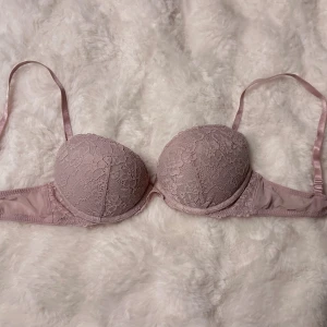 Ljuslila/rosa spets-bh från H&M 75B - Säljer en ljuslila eller rosa  bh från H&M i storlek 75B. Bh:n har vadderade kupor och är täckt med fin spets framtill. Axelbanden är justerbara och knäppningen bak har tre hakar. Materialet är mjukt och stretchigt för extra komfort.