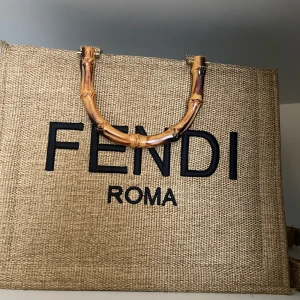 Beige shoppingväska  - Stilren shoppingväska  beige linnematerial med stora svarta. Väskan har snygga bambuinspirerade handtag och en matchande axelrem. Perfekt för dig som vill ha en trendig och rymlig väska med exklusiv känsla.