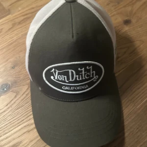 Von Dutch truckerkeps i svart och vitt - Snygg truckerkeps från Von Dutch med svart front och vit mesh på sidorna och bak. Broderad logga framtill och justerbar rem baktill för perfekt passform. Kepsen har klassisk böjd skärm och coolt California-tryck. Görfet keps som sitter otroligt fint bakomfram, pris går att diskutera vid snabba affär!