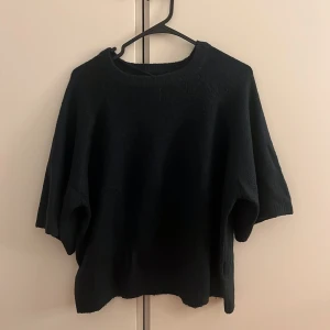 Svart stickad tröja från 157 - Svart stickad tröja från 157 med rund hals och breda, lite kortare ärmar. Tröjan har en loose passform och är perfekt för dig som gillar en enkel och stilren look. Materialet är mjukt och ger en skön känsla mot huden.