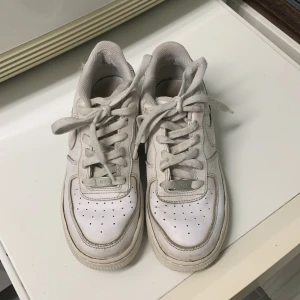 Nike Air Force 1 vita sneakers - Klassiska Nike Air Force 1 sneakers i helvitt skinn med perforerad tå och rund tå. Lågt skaft, snörning och ikonisk Nike Swoosh på sidan. Perfekta för dig som gillar streetstyle och tidlös design. Är ett litet hål på vänster sko på sulan där bak men det kommer inte in något vatten där 