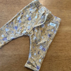 Blommiga leggings från Newbie - Supersöta byxor från Newbie i ljusgul ton med lila och vita blommor. Byxorna har snörning i midjan och är gjorda i mjuk bomull, perfekta för chill dagar. Blommigt mönster ger en gullig vibe och passformen är normal.