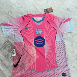 Barça x Nike rosa fotbollströja M - Säljer en FC Barcelona x Nike fotbollströja i en fet rosa färg med vita och blå detaljer. Tröjan har korta ärmar, V-ringad krage med turkos kant och coolt grafiskt mönster framtill. Materialet är lätt och andas, perfekt för match eller träning.