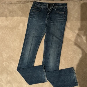Blå bootcut jeans från Acne Jeans - Snygga blå jeans från Acne Jeans med klassisk bootcut-modell. Jeansen har fem fickor, dragkedja och knapp framtill samt diskreta slitningar för en cool look. Tillverkade i mjukt denimtyg, de är midwaist och är i bra skick.