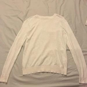 Vit tunn stickad tröja - En enkel och stilren vit stickad tröja med rund halsringning och långa ärmar. Tröjan är tunn och har en normal passform, perfekt att bära till jeans eller kjol. Materialet känns mjukt mot huden och ger en clean look.