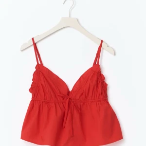 Röd linnetopp med knyt XS - Säljer en röd linnetopp i poplin med smala axelband och v-ringad hals. Toppen har en söt knytning framtill och lätt rynkade detaljer vid bysten. Perfekt för varma dagar och enkel att styla med jeans eller kjol.