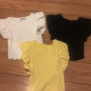 Tre volangtoppar  - Säljer tre snygga toppar med volangärmar i färgerna vit, svart och ljusgul. Priset gäller för alla tre alltså 30 kr. 