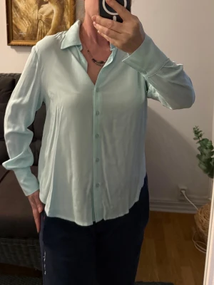 Ljusblå Tilda skjorta i viscose. - Snygg mintgrön skjorta från Tilda med klassisk krage och knappar framtill. Skjortan är tillverkad i viscose och har lång ärm med enkel manschett. Perfekt för en clean och fräsch look. Ledig passform.