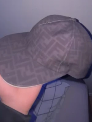 Grå Fendi keps med FF-mönster - Säljer en grå keps från Fendi med det klassiska FF-logomönstret över hela kepsen. Kepsen har böjd skärm och är tillverkad i ett tygmaterial som känns både stilrent och lyxigt. Perfekt accessoar för dig som vill sticka ut med designerplagg.