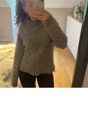 Mörkgrå stickad tröja med polokrage - Mysig mörkgrå stickad tröja med polokrage och långa ärmar. Tröjan har en avslappnad passform och ribbstickade muddar vid ärmslut och nederkant. Perfekt för kyliga dagar och enkel att matcha med jeans eller kjol.