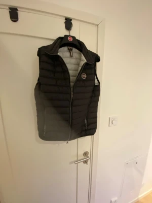 Svart dunväst från Colmar - Snygg svart dunväst från Colmar med quiltad design och hög krage. Västen har dragkedja framtill, två sidofickor med dragkedja och Colmar-logga på bröstet. Perfekt för lager-på-lager och håller dig varm under kyliga dagar.