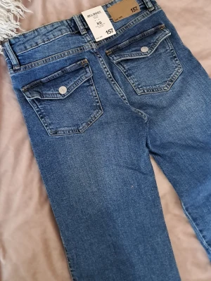 Blå bootcut jeans från 157 XS - Bootcut jeans i klassisk blå denim från 157. Modellen har fem fickor, snygga bakfickor med lock och silverfärgade knappar. Jeansen har normalhög midja och är tillverkade i ett stretchigt material för skön passform.