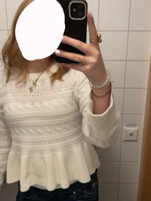 Vit stickad peplumtröja - Säljer en vit stickad tröja med peplumvolang och fina stickade mönster. Tröjan har rund halsringning och långa ärmar. Perfekt för dig som gillar en söt och trendig stil.