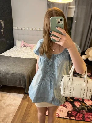 Ljusblå blus från generous denim by lindex  - Söt ljusblå blus från generous denim by lindex med korta ärmar och rundad halsringning. Blusen har dekorativa knappar framtill och fina rynkade detaljer vid axlar och hals. Tillverkad i mjuk denim. Storlekar M. Skriv om funderingar och priset kan diskuteras 