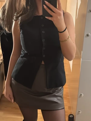 Kort svart kjol i skinnimitation - Snygg kort brun kjol i skinnimitation med slät yta och figurnära passform. Perfekt för dig som gillar en stilren och trendig look. Kjolen har en enkel design utan synliga detaljer och passar till många olika outfits. Använd en gång. 