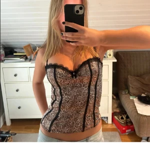 Leopardmönstrad korsettopp - Trendig leopardmönstrad korsettopp med svarta spetsdetaljer. Inbyggd bh. Storlek s