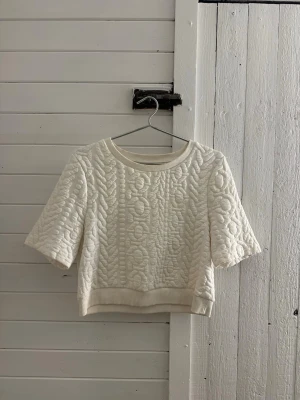 Vit quiltad croppad topp - Supersnygg vit croppad topp med quiltat mönster och korta ärmar. Rund halsringning och ribbade kanter ger en clean look. Perfekt att styla med höga jeans eller kjol för en trendig vibe.