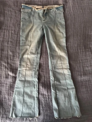 Ljusblå bootcut jeans med rå kant - Super snygga och trendiga bootcut jeans med låg midja. Kanten är fransig och gör jeansen extra snygga och unika. De är i väldigt bra skick och sitter jätte skönt då materialet inte är för stretchigt och inte heller för hårt. Fråga gärna om mått!