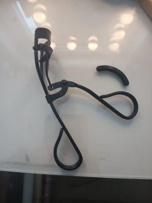 Svart ögonfransböjare i metall - En stilren svart ögonfransböjare i metall med ergonomiska handtag och utbytbar silikonkudde. Perfekt för att skapa snygg böj på fransarna. Medföljer en extra silikonkudde för längre användning.