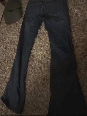 Mörkblå bootcut jeans - Säljer ett par mörkblå bootcut jeans med klassisk femficksdesign och normal midja. Jeansen har utsvängda ben och är tillverkade i ett mjukt denimtyg som ger en avslappnad look. Perfekta för dig som gillar retrostil och vill ha ett par bekväma jeans.