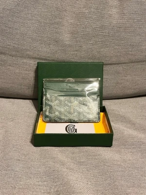 Grön kortplånbok från G@yard - Snygg och stilren kortplånbok från G i grön färg med klassiskt mönster och diskret logga framtill. Plånboken är tillverkad i canvas och läder, har flera kortfack och levereras i originalask med tillbehör.