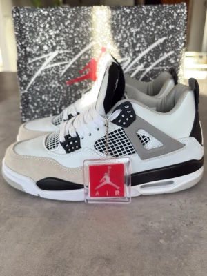 Air Jordan 4 OG Military Black - Snygga Air Jordan 4 OG Military Black sneakers med vit och grå ovandel i läder och mocka, svarta detaljer och klassiskt mesh på sidorna. Ikonisk siluett med synlig Air-enhet i sulan och coola plastdetaljer. Perfekta för dig som gillar streetwear och basketstil.