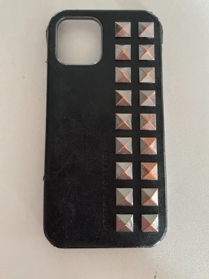 Svart mobilskal med nitar från iDeal - Snyggt svart läder mobilskal från iDeal of Sweden med två rader fyrkantiga metallnitar i guld och silver på baksidan. Skalet har en stilren design och är gjort i hårdplast som skyddar mobilen samtidigt som det ger en cool look.