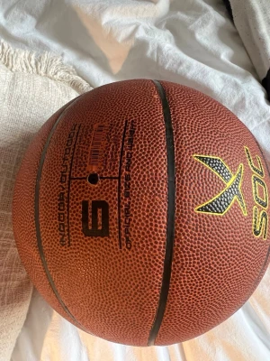 Basketboll från SOC CGL - Brun basketboll från SOC med CGL-tryck i guld och svart logga. Bollen har klassisk texturerad yta och svarta linjer. Passar både inomhus och utomhusspel. Materialet är syntetiskt gummi.