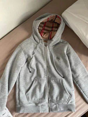 Burrbery zip hoodie  - Säljer en grå burrbery zip som har väldigt snygga mönster vid huvan och inuti har det väldigt skön vit päls som värmer en riktigt bra på vintern och man kan justera med snören. Kontakta gärna om ni är intresserad ☺️