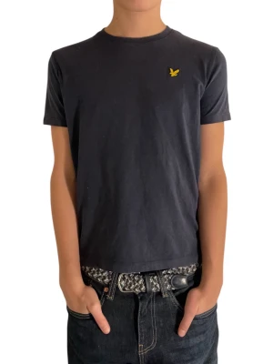 mörkblå t-shirt från Lyle & Scott  - En mörkblå t-shirt från Lyle & Scott med klassisk passform och rund hals. T-shirten har en liten gul logga broderad på bröstet och är tillverkad i mjuk bomull. Perfekt för en clean och stilren look. Modellen är 167