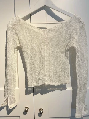 Vit långärmad spets topp med struktur - Säljer en vit långärmad topp med off shoulder-skärning och strukturerat, lite bubbligt tyg. Tröjan har en croppad passform och knappar vid ärmslutet.  Perfekt för dig som gillar en trendig och unik stil.