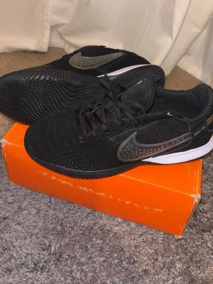 Nike Street Gato svarta sneakers - Snygga svarta Nike Street Gato sneakers med svart ovandel i mesh och mocka, samt en vit sula. Skorna har en stor grå Nike Swoosh med prickigt mönster på sidan och svarta skosnören. Perfekta för dig som gillar sportig och stilren look. Tveka inte på att slå en pling 🤝🤩