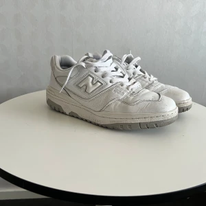 Vita New Balance 550 sneakers - Snygga vita New Balance 550 sneakers med klassisk siluett och grå detaljer. Skorna har en låg profil, robust sula och är tillverkade i en mix av läder och syntetmaterial. Perfekta för dig som gillar retrostil och streetwear.