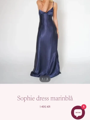 Marinblå långklänning Sophie dress - Snygg marinblå långklänning från By Stina i glansigt material med smala axelband och v-ringad urringning. Klänningen har en elegant och enkel siluett som faller mjukt längs kroppen. Perfekt för dig som vill ha en stilren look. Klänningen är helt ny med prislapp på.