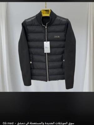 Svart dunjacka från Dior - Snygg svart dunjacka från Dior med quiltad front och släta ärmar. Jackan har ståkrage, dragkedja framtill och diskret Dior-logga på bröstet. Perfekt för kalla vinterdagar och ger en stilren look. 