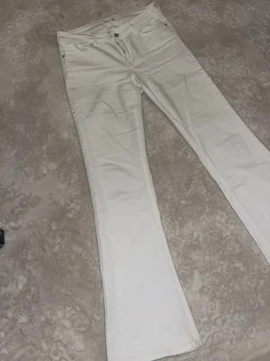 Vita bootcut jeans från Lindex - Säljer ett par vita bootcut jeans från ”bylindex”. Jeansen har klassisk femficksdesign, normal midja och utsvängda ben. Perfekta för dig som vill ha en fräsch och stilren look. Materialet är bomull med lite stretch för extra komfort.