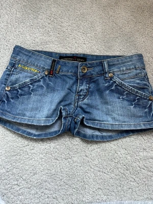Lågmidjade blå jeansshorts  - Snygga blå jeansshorts från Musketeer med låg midja och slitna detaljer. 