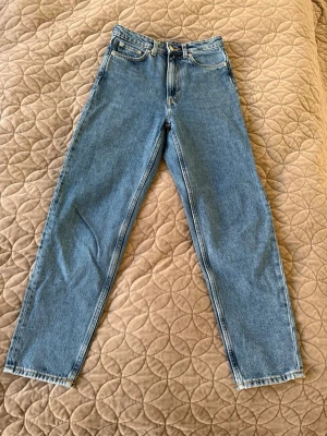 Blå raka jeans från LASH - Snygga blå jeans från LASH med klassisk rak passform och hög midja. Tillverkade i slitstarkt denimtyg med fem fickor och dragkedja med knapp. Perfekta för en avslappnad och trendig look.