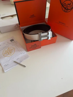  vitt skärp med silver H-spänne - Säljer ett stilrent vitt skärp som man kan byta sida på med ikoniskt H-spänne i silverfärgad metall. Skärpet är tillverkat i exklusivt skinn och levereras i originalförpackning. Perfekt accessoar för att lyfta vilken outfit som helst.