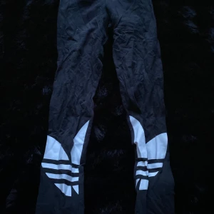 Svarta träningsbyxor från Adidas - Snygga svarta träningsbyxor från Adidas med vita detaljer och den klassiska loggan på benen. Perfekta för träning eller en avslappnad dag. Byxorna har en bekväm passform och är tillverkade i ett mjukt material.