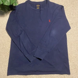 Mörkblå långärmad tröja från Ralph Lauren - Säljer en stilren mörkblå långärmad tröja från Ralph Lauren med det klassiska röda broderade logotypen på bröstet. Perfekt för en avslappnad och snygg look. Tröjan är i storlek S och har en bekväm passform. Priset kan gå ner