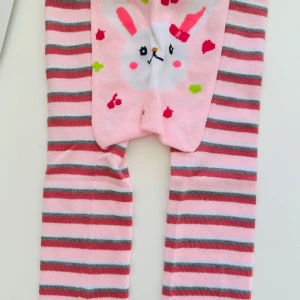 Randiga barn-leggings med kaninmotiv - Söta strumpbyxor för barn med randigt mönster i rosa, grått och vitt. Baken pryds av ett gulligt kaninmotiv med rosa kinder och öron. Perfekta för att ge en lekfull touch till vardagsoutfiten. Storlek 90, 1-2 år. 