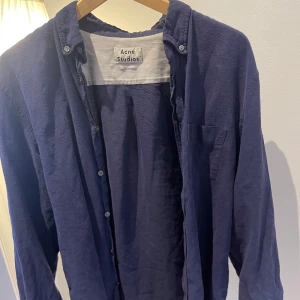 Mörkblå skjorta från Acne Studios - Säljer en stilren mörkblå skjorta från Acne Studios i klassisk passform. Skjortan har långa ärmar och knappar framtill. Perfekt för en avslappnad men ändå snygg look.