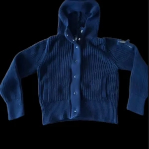 Mörkblå stickad hoodie med dragkedja - Säljer en snygg mörkblå stickad hoodie med dragkedja och knappar. Den har en mysig huva och ribbade detaljer som ger en cool look. Perfekt för kyliga dagar!